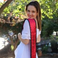 Avery Cochrane - woman in white wearing graduation sash smiles looking over shoulder